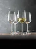 Four wine glasses are arranged on a wooden surface against a textured gray background. One glass contains white wine. Náhled obrázku produktu