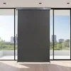 A dark gray roller blind is installed on a large window overlooking a city skyline and greenery. Náhľad obrázku produktu