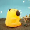 A yellow, bear-shaped night light sits on a sandy beach next to two small bottles. Náhľad obrázku produktu