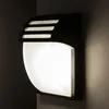 A black outdoor wall light with a frosted glass diffuser, mounted on a gray wall in a corner. Produktbild-Vorschau