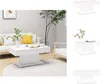 A white coffee table is placed in a modern living room setting with a sofa, armchair, and a plant. Náhled obrázku produktu