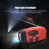 A red and black emergency hand-crank radio with a flashlight is shown in a camping scene at night, with a tent and two people in the background. The flashlight beam illuminates the scene. Podgląd zdjęcia produktu