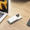 A white power bank is attached to a gold smartphone, which is placed on a wooden desk next to a laptop. Náhled obrázku produktu