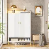 A white shoe cabinet with gold accents is shown in an entryway, next to a window and a door. A small tan ottoman with a gray blanket is placed to the right of the cabinet. The cabinet has two doors and a lower shelf displaying shoes and a box. Several pair Náhľad obrázku produktu