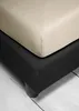 A close-up view of a bed base covered in black fabric with a beige fitted sheet on top. Produktbild-Vorschau