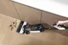 A person is using a Tineco FLOOR ONE S7 Premium wet and dry vacuum cleaner to clean up dirt on a wooden floor next to kitchen cabinets. Náhled obrázku produktu