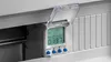 A digital timer with a clear protective cover is mounted on a DIN rail inside a panel. Náhled obrázku produktu