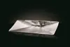 A silver-colored grease tray is shown on a reflective black surface with a dark background. Produktbild-Vorschau