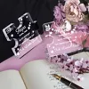 Two puzzle-shaped decorations, one black and one pink, are placed on a pink surface next to an open book and a bouquet of flowers. A pen rests on the book. Náhľad obrázku produktu