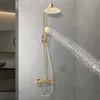 A gold shower system with a rain showerhead and handheld showerhead is shown against a gray tiled wall. Náhled obrázku produktu