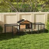 A rabbit hutch with an attached run is set up on a grassy lawn in front of a wooden fence. Produktbild-Vorschau
