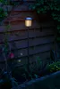 A solar garden light illuminates a garden at dusk, with flowers and a wooden fence in the background. Produktbild-Vorschau