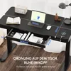A black standing desk with various items on it, including a laptop, books, and a phone charging. Náhled obrázku produktu