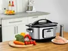 A multi-cooker is shown on a kitchen counter with fresh ingredients and raw chicken. Produktbild-Vorschau