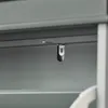 A close-up view of a metal bracket with a dark plastic piece attached, mounted on the underside of a shelf. Podgląd zdjęcia produktu