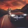 A silver car driving on a road at sunset with a city skyline in the background. Produktbild-Vorschau
