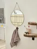 A bathroom scene with a round mirror, a towel hanging on a hook, and a shelf with toiletries and a small bear figurine. Produktbild-Vorschau