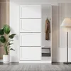 A modern white shoe cabinet with a mirror on the right side, placed in a room with a plant and a floor lamp. Náhľad obrázku produktu