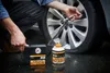 A person is using a tire sealant kit to repair a car tire on a wet surface. Produktbild-Vorschau