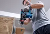 A man is using a cordless hammer drill to drill into a piece of wood. Produktbild-Vorschau