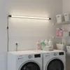 A laundry room with washing machines, shelves with cleaning supplies and baskets, and a linear LED light fixture mounted on the wall. Náhľad obrázku produktu