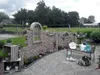 A garden scene with a decorative brick wall, a bench, and various garden ornaments. Produktbild-Vorschau