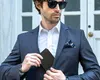 A man in a suit is putting a wallet into his suit pocket. Anteprima dell’immagine prodotto