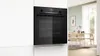 A built-in black oven is shown in a white kitchen cabinet, with a dining room visible through a doorway on the right. Produktbild-Vorschau