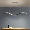 A modern LED pendant light hangs above a wooden table with a book and a bowl on it. Produktbild-Vorschau
