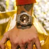 Close-up of a person's wrist wearing a transparent G-Shock watch with a bronze dial, against a blurred gold background. Voir les images du produit