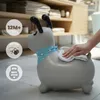 A gray dog-shaped inflatable toy is being wiped with a cloth in a room with shelves in the background. Produktbild-Vorschau