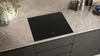 A modern kitchen countertop with a black induction hob, marble-effect countertop, and dark cabinets. Náhľad obrázku produktu