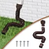 A brown flexible downspout extension attached to a white downspout, curving down onto green grass next to a white brick wall. A separate set of the downspout extension components and screws are shown in the lower right corner. Náhled obrázku produktu