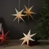 Several paper star lanterns are displayed in a room, with a Christmas tree in the background. Podgląd zdjęcia produktu
