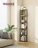 A tall, narrow corner bookshelf is filled with decorative items and storage boxes, placed in a living room next to a couch and a large plant. The bookshelf has a rustic brown wood finish and black metal framing. Produktbild-Vorschau