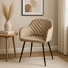 A beige upholstered dining chair with black metal legs is placed next to a small wooden side table with a vase of dried pampas grass and books. Náhľad obrázku produktu