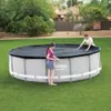 Two people are covering a round swimming pool with a black cover. Produktbild-Vorschau