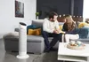 A couple holding hands on a couch in a living room, with a white tower fan in the foreground. Voir les images du produit