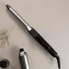 A curling iron, hairpins, and a can of hairspray are laid out on a neutral surface. Náhled obrázku produktu