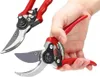 A hand holding a pair of red and silver garden shears, with another pair of shears in the background. Podgląd zdjęcia produktu