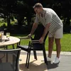 A man is adjusting a chair at an outdoor dining table. Produktbild-Vorschau