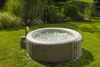 An inflatable hot tub filled with bubbling water sits on a green lawn surrounded by lush vegetation. Produktbild-Vorschau