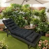 A black lounge cushion on a chaise lounge chair in a lush garden setting with an umbrella overhead. Náhled obrázku produktu