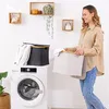 A woman is holding a laundry basket next to a washing machine, with shelves and plants in the background. Produktbild-Vorschau
