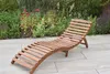 A wooden lounger is placed on a patio in front of a garden with various plants and flowers. Náhled obrázku produktu
