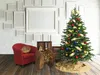 A decorated Christmas tree stands next to a red armchair in a room with a white brick wall and many empty picture frames. Produktbild-Vorschau