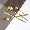 A set of gold cutlery arranged on a textured placemat and a white surface. Produktbild-Vorschau
