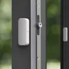 A close-up shot of two white smart home sensors attached to a dark gray door or window frame, with a blurred green background. Anteprima dell’immagine prodotto