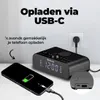 A black Denver radio alarm clock is shown charging a smartphone via a USB-C cable. The clock displays the time 12:00. Podgląd zdjęcia produktu