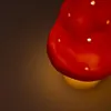 A close-up shot of a red mushroom-shaped lamp with small white dots, emitting a warm yellow light. Produktbild-Vorschau